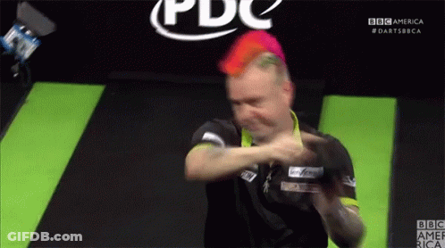 A Man With Red Hair Is Playing Darts In Front Of A BBC America Logo GIF