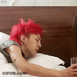 A Man With Red Hair Is Sleeping On A Bed While Looking At His Phone . GIF