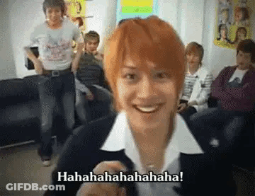 A Man With Red Hair Is Smiling In Front Of A Group Of People In A Room . GIF