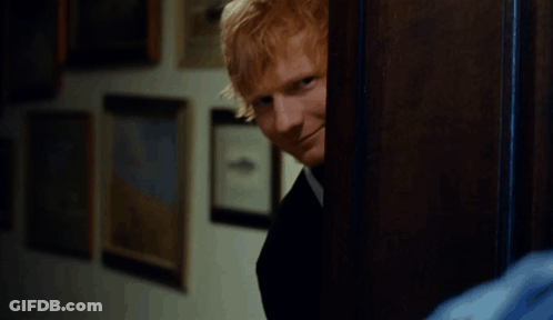 A Man With Red Hair Is Smiling While Peeking Out Of A Doorway GIF