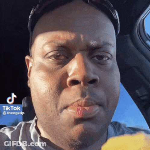 A Man With Red Lipstick On His Lips Is Sitting In A Car Eating A Piece Of Food . GIF