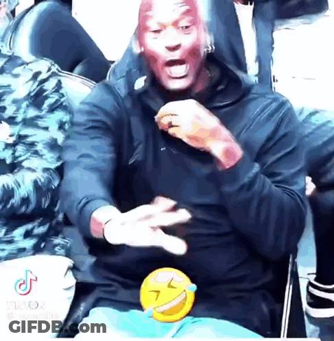 A Man With Red Paint On His Face Is Sitting In A Chair With A Smiley Face On His Lap . GIF