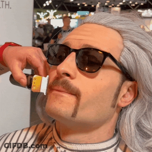 A Man With Sunglasses And A Mustache Is Getting His Beard Trimmed GIF