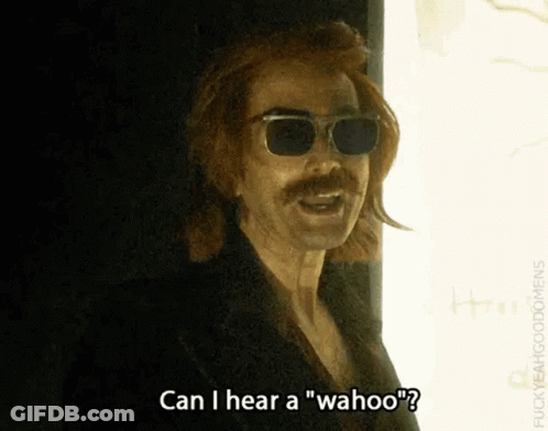 A Man With Sunglasses And A Mustache Is Standing In Front Of A Window And Talking . GIF