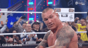 A Man With Tattoos Is Standing In A Wrestling Ring With A Crowd Watching . GIF