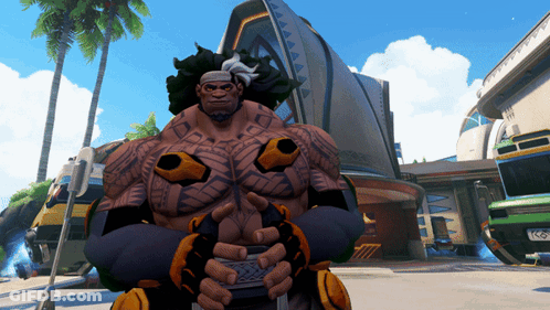 A Man With Tattoos On His Arms And Chest Stands In Front Of A Building GIF