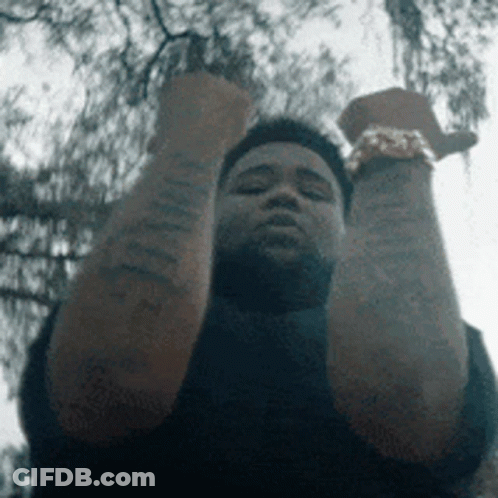A Man With Tattoos On His Arms Is Holding His Fist Up In The Air . GIF