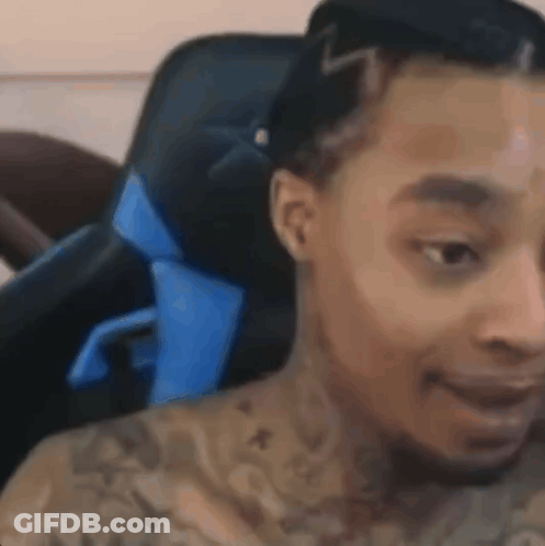 A Man With Tattoos On His Chest Is Sitting In A Chair . GIF