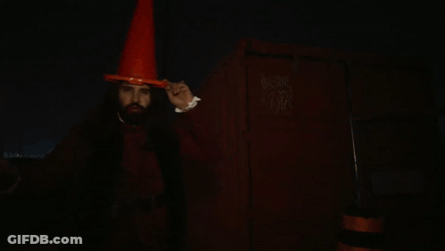 A Man With Vampire Teeth Wearing An Orange Cone Hat GIF