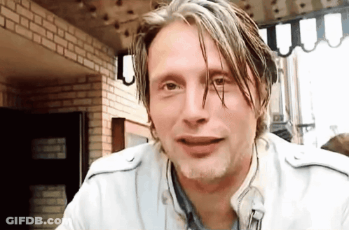 A Man With Wet Hair Is Sitting In Front Of A Brick Wall And Looking At The Camera . GIF
