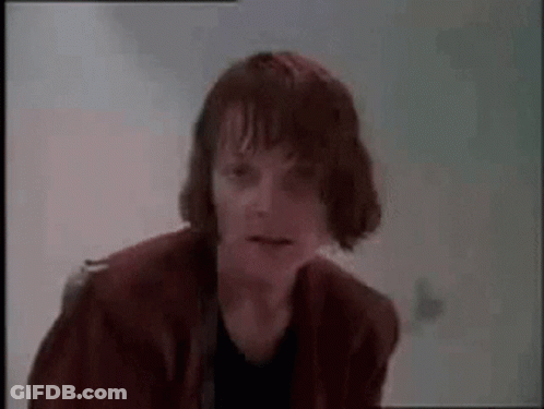 A Man With Wet Hair Is Standing In Front Of A White Wall And Making A Funny Face . GIF