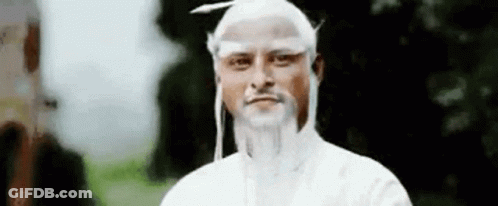 A Man With White Hair And A Beard Is Standing In Front Of A Tree And Looking At The Camera . GIF