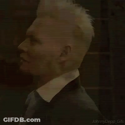 A Man With White Hair Is Wearing A Black Suit And Tie . GIF