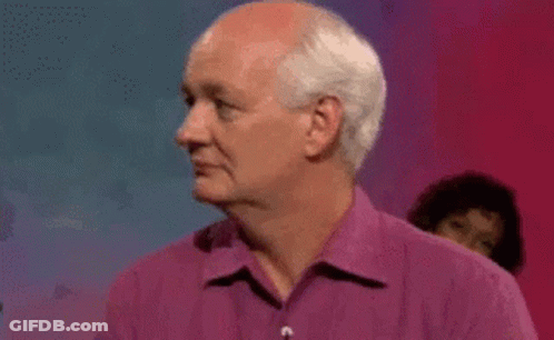 A Man With White Hair Is Wearing A Purple Shirt And Looking To The Side . GIF