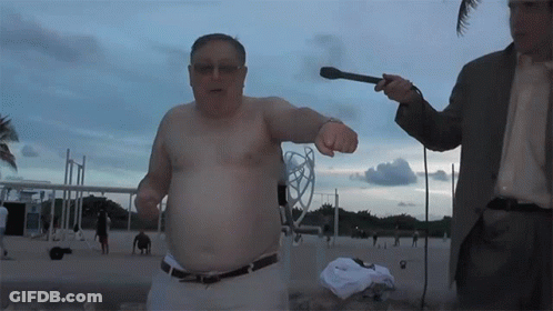 A Man Without A Shirt Is Being Interviewed By A Man In A Suit Holding A Microphone GIF