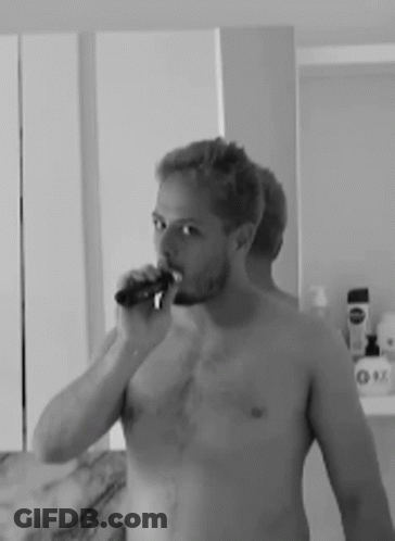 A Man Without A Shirt Is Brushing His Teeth In Front Of A Mirror . GIF