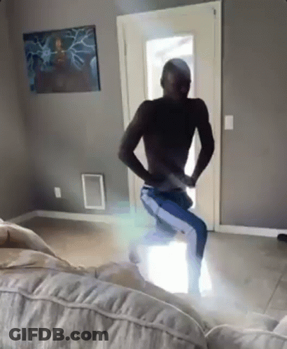A Man Without A Shirt Is Dancing In A Living Room With A Couch . GIF