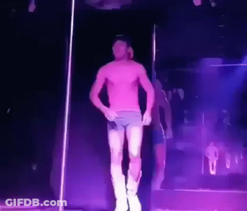 A Man Without A Shirt Is Dancing On A Pole In A Dark Room GIF