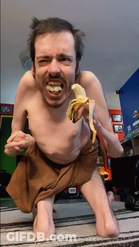 A Man Without A Shirt Is Eating A Banana On The Floor GIF