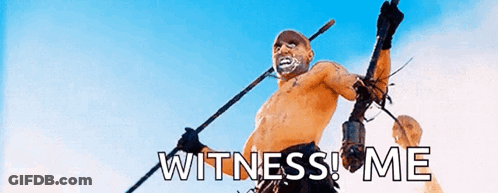 A Man Without A Shirt Is Holding A Spear With The Words Witness Me Written On It . GIF