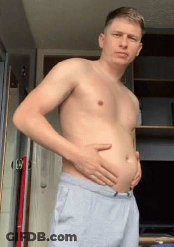 A Man Without A Shirt Is Holding His Belly In Front Of A Door GIF