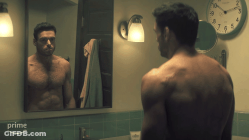 A Man Without A Shirt Is Looking At Himself In A Bathroom Mirror With A Clock On The Wall Above Him That Says Prime GIF