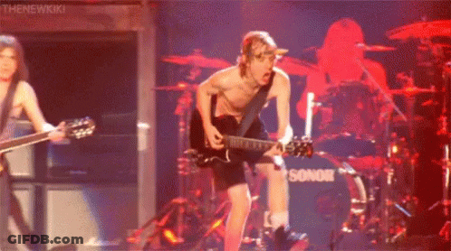 A Man Without A Shirt Is Playing A Guitar On Stage In Front Of A Drum Set . GIF