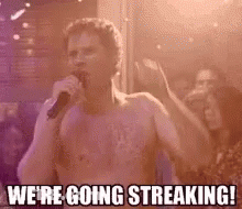 A Man Without A Shirt Is Singing Into A Microphone In Front Of A Crowd . GIF