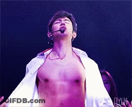 A Man Without A Shirt Is Singing Into A Microphone On A Stage GIF