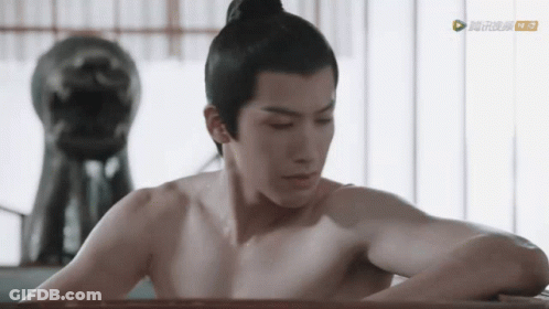 A Man Without A Shirt Is Sitting In A Bathtub With A Statue In The Background GIF