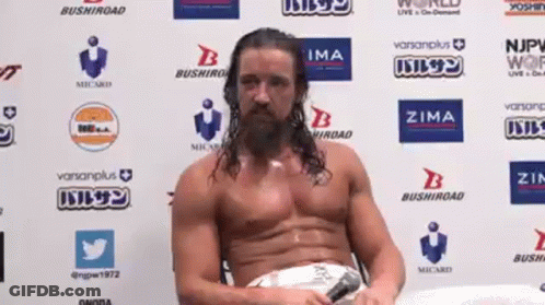A Man Without A Shirt Is Sitting In Front Of A Wall With Logos On It GIF