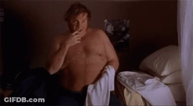 A Man Without A Shirt Is Sitting On A Bed With A Towel Around His Waist GIF