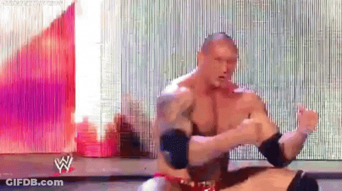 A Man Without A Shirt Is Sitting On A Stage In Front Of A Large Screen With The Letter W On It . GIF
