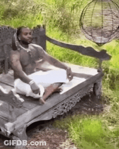 A Man Without A Shirt Is Sitting On A Wooden Bench In The Woods . GIF