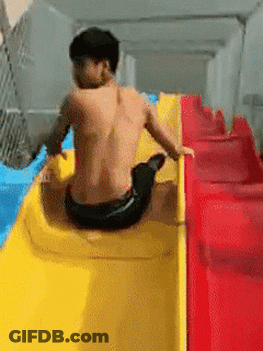 A Man Without A Shirt Is Sitting On A Yellow And Red Slide GIF