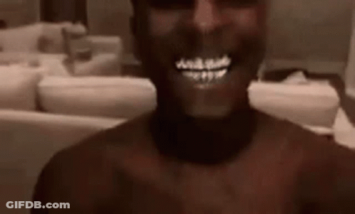 A Man Without A Shirt Is Smiling In A Living Room . GIF