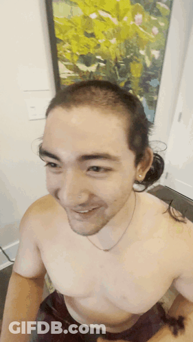 A Man Without A Shirt Is Smiling In Front Of A Picture GIF