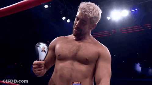 A Man Without A Shirt Is Standing In A Boxing Ring Holding A Trophy . GIF