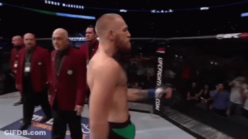 A Man Without A Shirt Is Standing In A Boxing Ring With His Arms Outstretched . GIF
