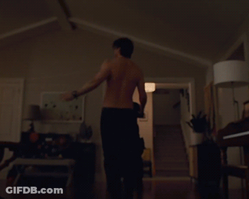 A Man Without A Shirt Is Standing In A Dark Room GIF