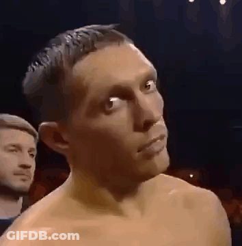 A Man Without A Shirt Is Standing In A Dark Room With A Man In The Background . GIF