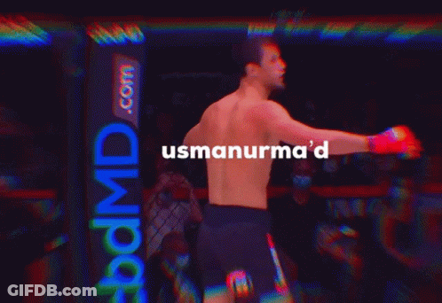 A Man Without A Shirt Is Standing In A Dark Room With The Words Usmanurma 'D Above Him GIF