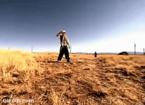 A Man Without A Shirt Is Standing In A Field Of Dry Grass . GIF
