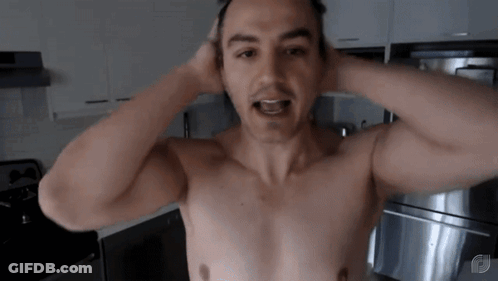 A Man Without A Shirt Is Standing In A Kitchen With His Hands On His Head . GIF