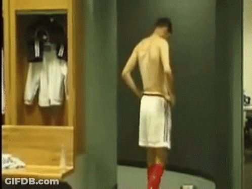 A Man Without A Shirt Is Standing In A Locker Room With A Towel Around His Waist . GIF