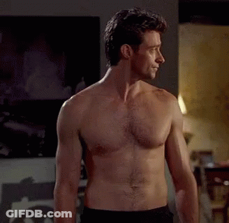 A Man Without A Shirt Is Standing In A Room . GIF