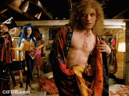 A Man Without A Shirt Is Standing In A Room Surrounded By People GIF