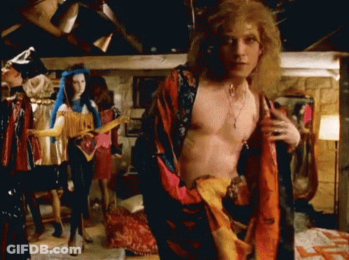 A Man Without A Shirt Is Standing In A Room With Clothes On Display . GIF