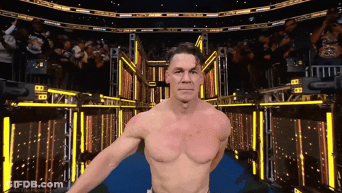 A Man Without A Shirt Is Standing In A Stadium With A Crowd Behind Him GIF