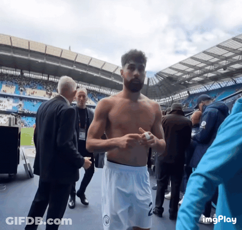 A Man Without A Shirt Is Standing In A Stadium With A Man In A Suit Standing Behind Him GIF